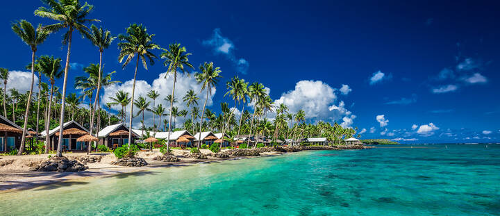 A stunning view of Samoa's lush landscape, featuring vibrant green foliage, palm trees, and clear turquoise waters. The image showcases a beautiful beach with soft sand, inviting visitors to relax and enjoy the tropical paradise and its natural beauty.