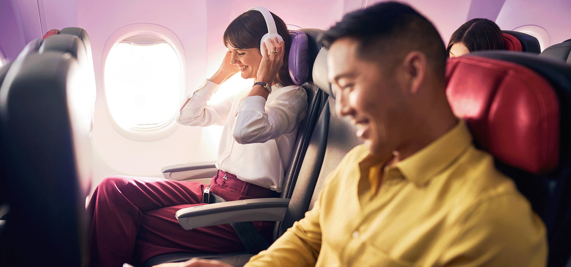 Guests travelling on Virgin Australia flight sitting in cabin with headphones on listening to music.