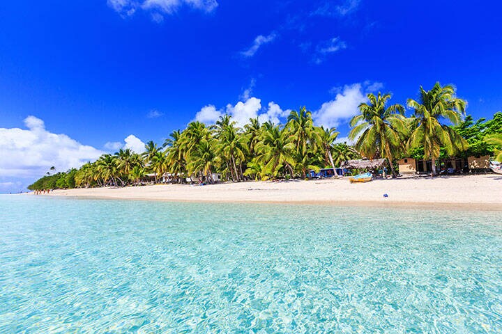 Beach on tropical Dravuni Island, Fiji with clear blue water, white sane and green palm trees