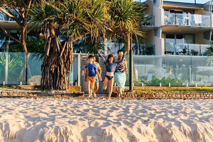 Family running on the beach towards the ocean at Noosa Heads Main Beach