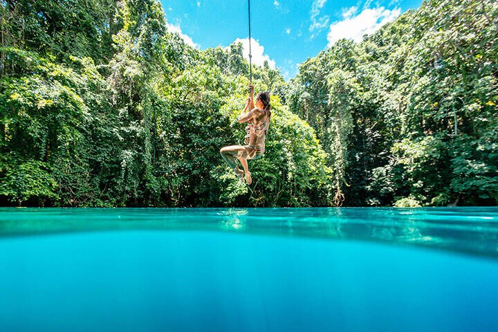 A woman on a rope swing over Riri Blue Hole, Espiritu Santo, Vanuatu 